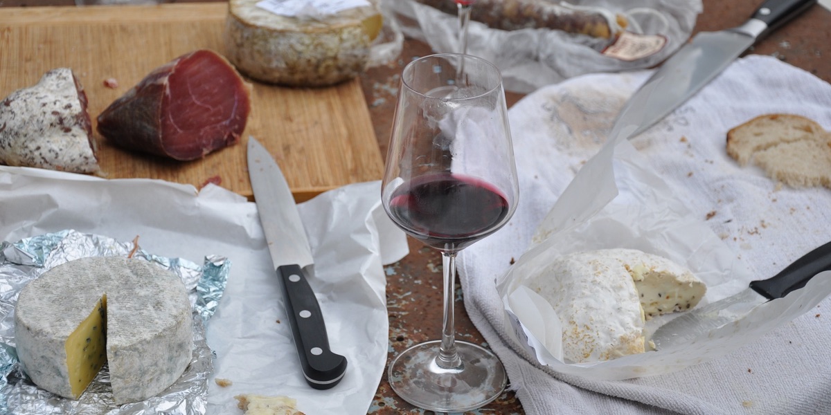 a half-finished board of mixed cheeses, charcuterie, and red wine
