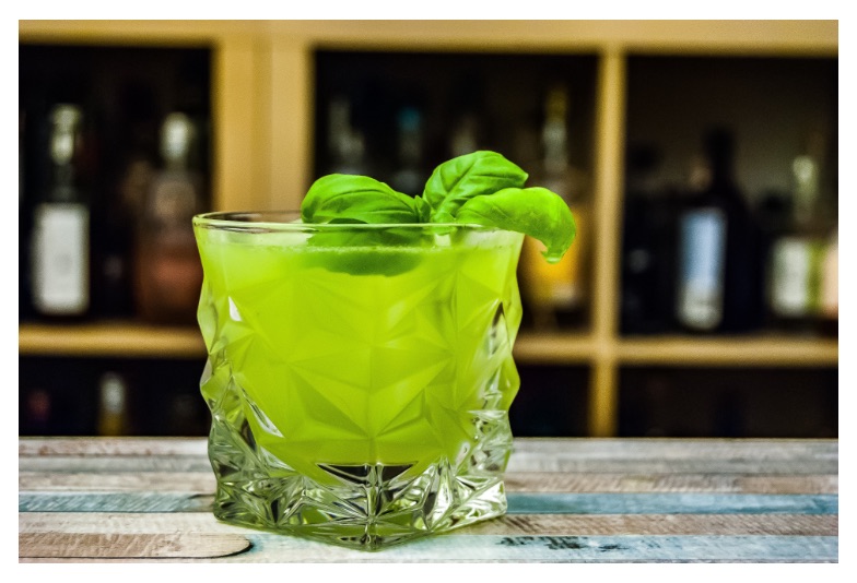a bright green cocktail topped with basil